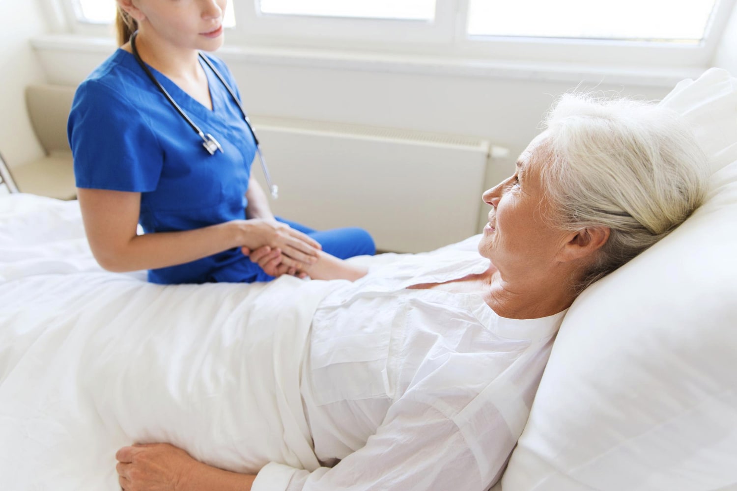 Pielęgniarka siedząca przy łóżku starszej kobiety